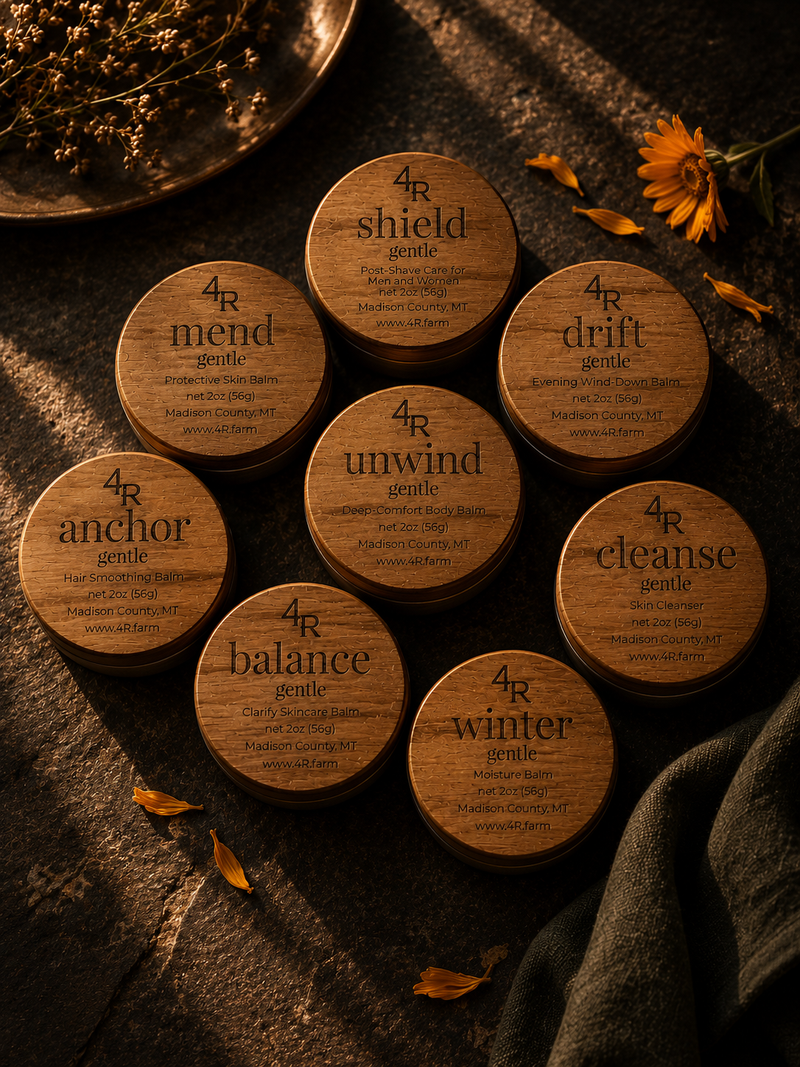 Eight 4R Farm GENTLE Care balms arranged with botanicals on a dark wooden table