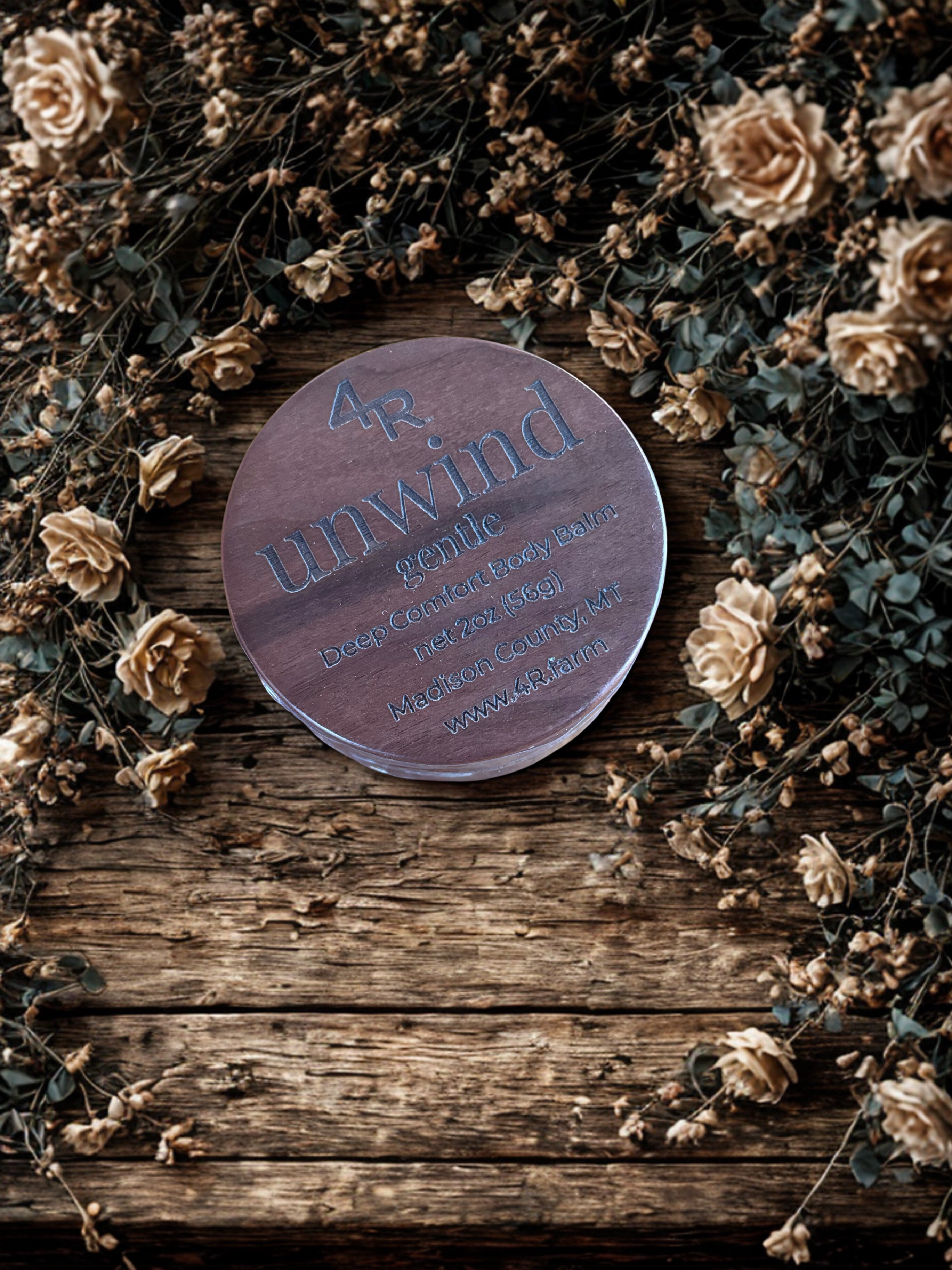Wooden jar of 4R Farm UNWIND: Gentle on a rustic wooden table surrounded by flowers.