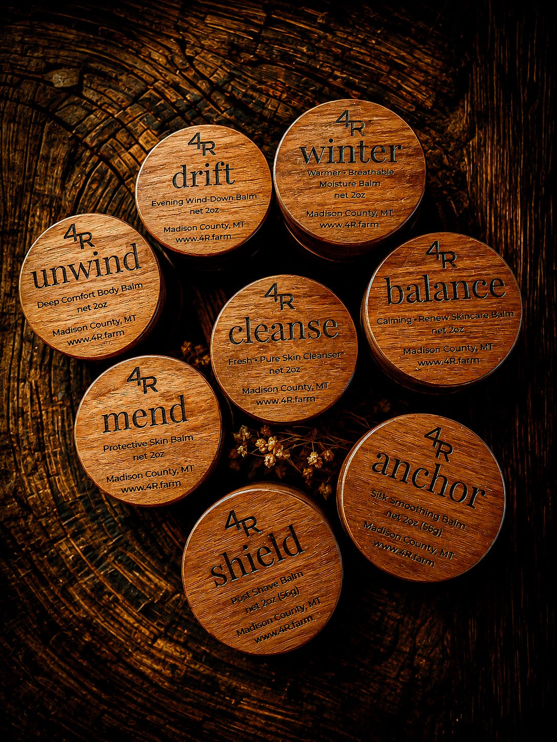 8 wooden containers of 4R Farm botanical wellness balms on a wooden background.