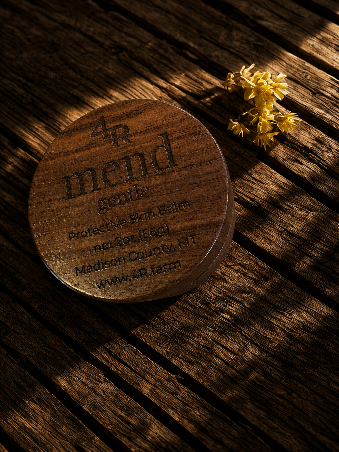 Dark wooden container of 4r gentle care balm on a wooden surface with yellow flowers.