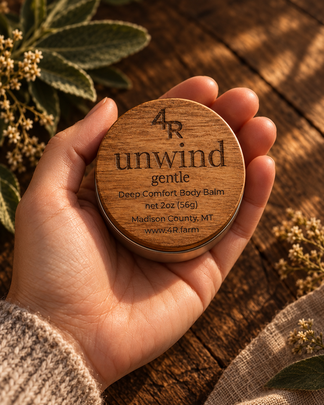 Hand holding UNWIND GENTLE Deep Comfort Body Balm in its walnut-lidded tin