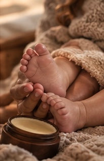 Baby’s feet resting beside an open container of MEND Protective Skin Balm.