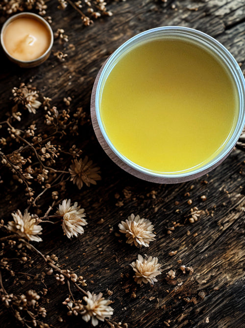 Jar of yellow cream on a wooden surface with dried flowers