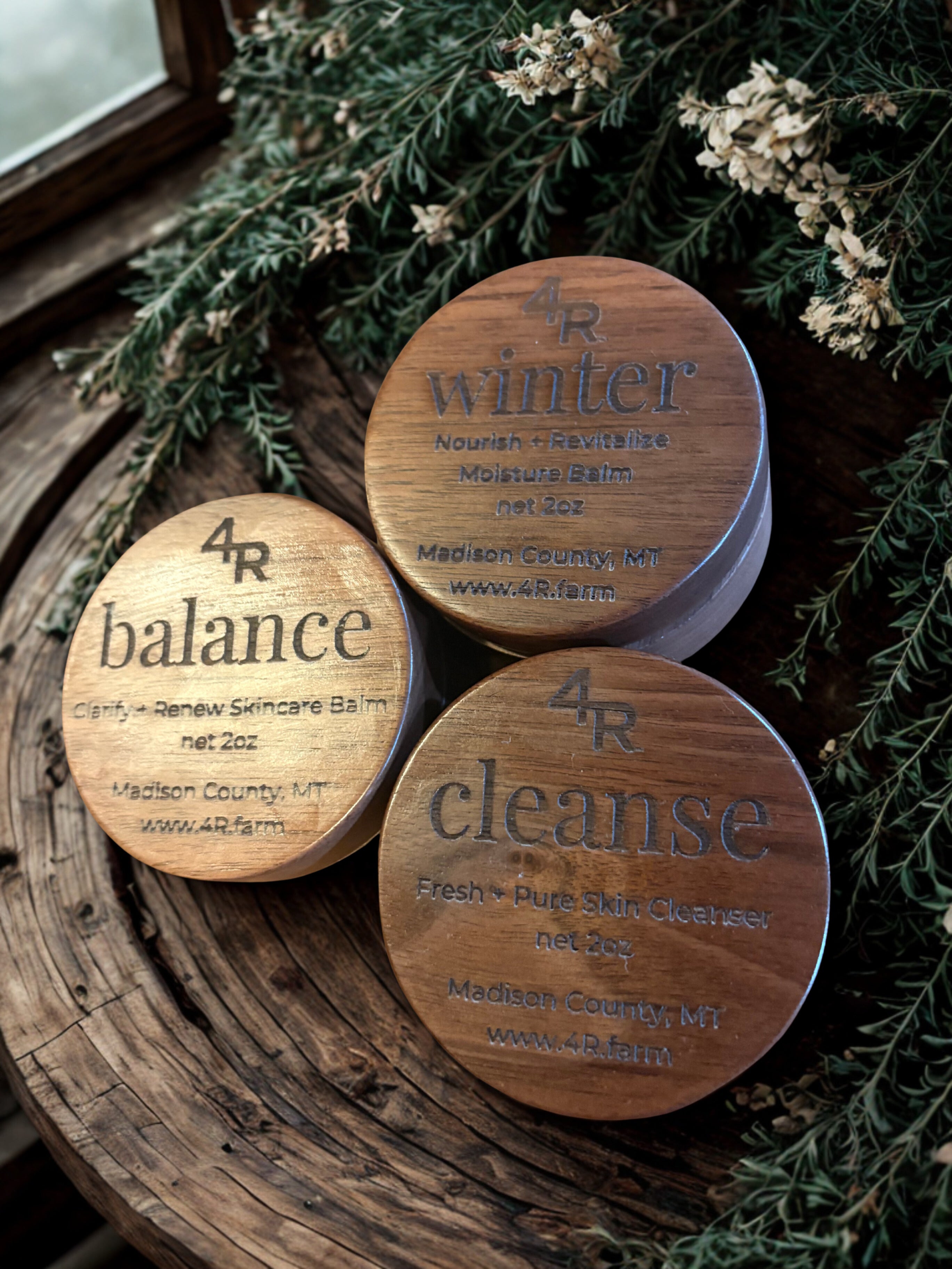 Three wooden containers labeled 'balance', 'winter', and 'cleanse' on a rustic surface with greenery.