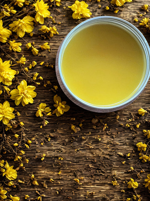 Yellow balm in a wooden and metal tin surrounded by yellow flowers on a wooden surface