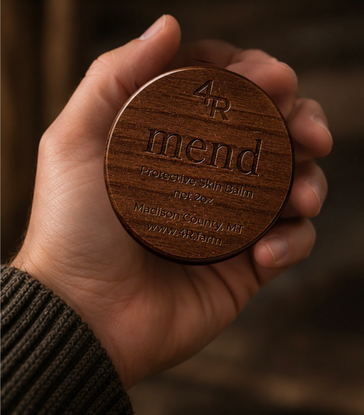 Hand holding MEND Protective Skin Balm in its walnut container.