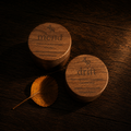 Two round wooden tins labeled 'merid' and 'drift' by 4R Farm, arranged on a dark wood surface with a small dry leaf beside them.