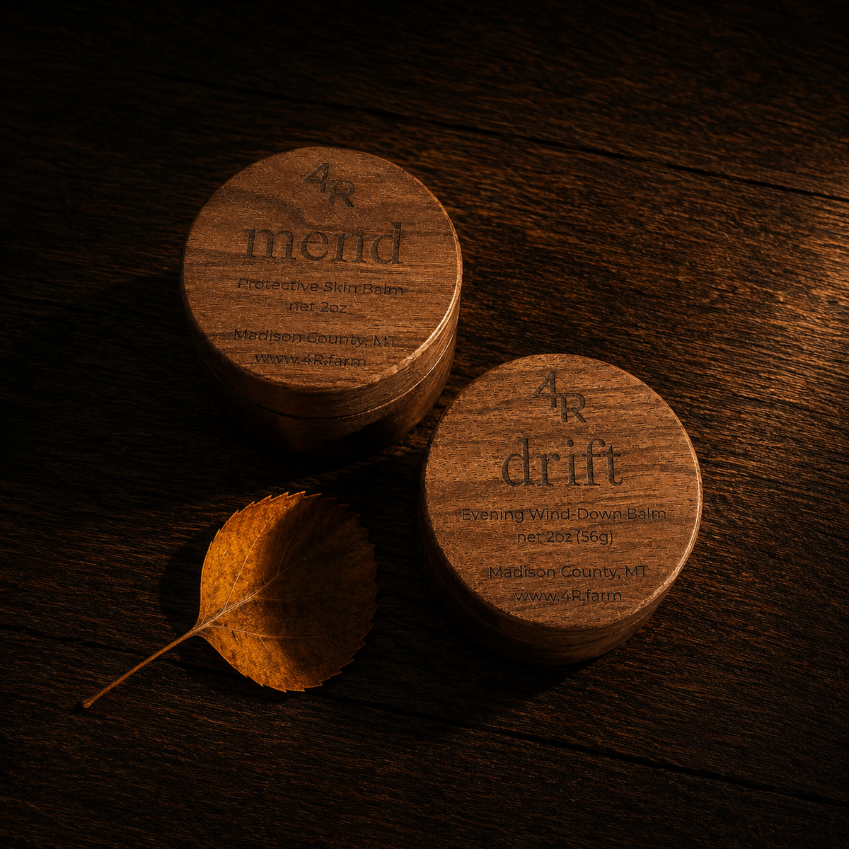 Two round wooden tins labeled 'merid' and 'drift' by 4R Farm, arranged on a dark wood surface with a small dry leaf beside them.