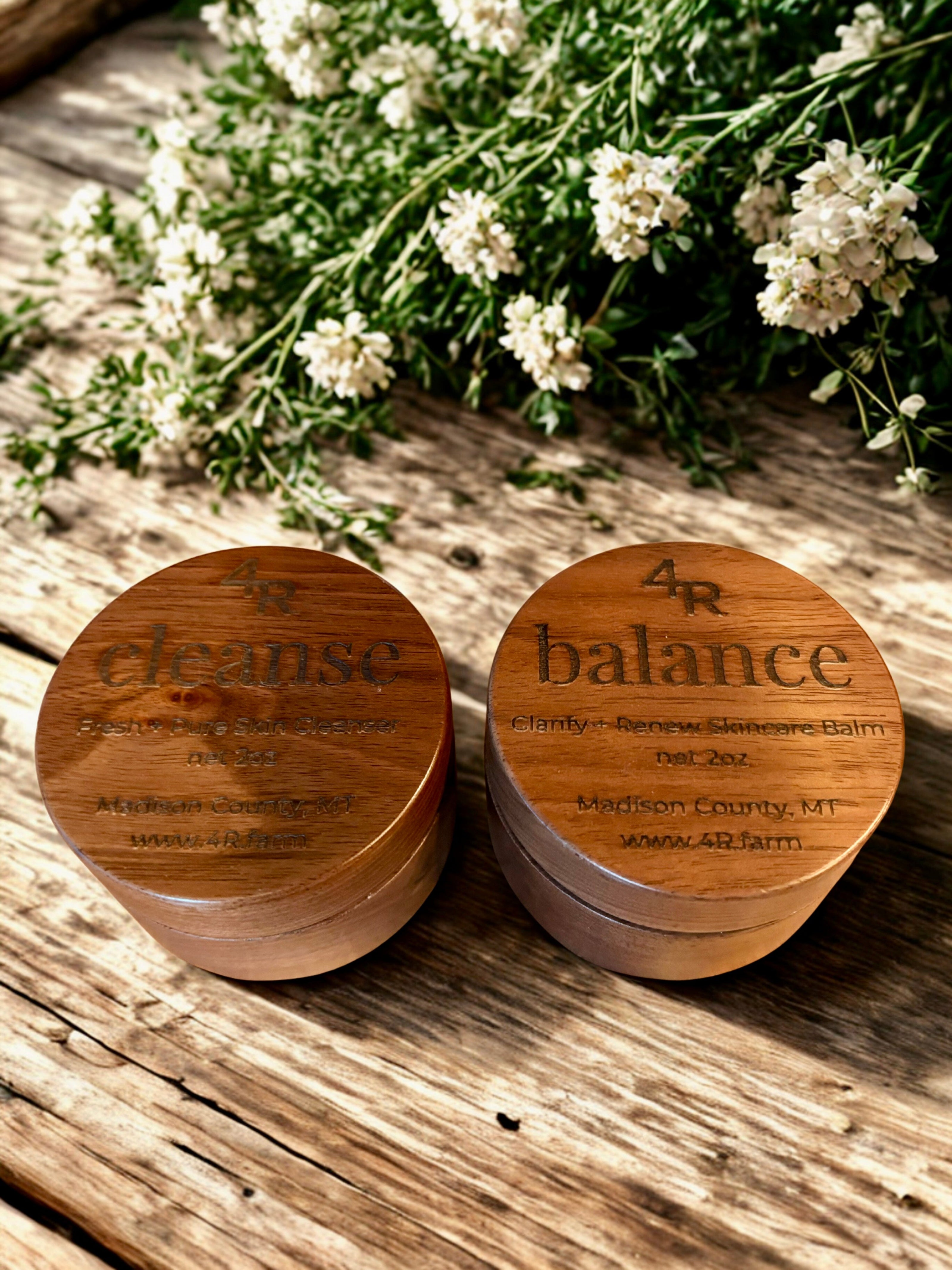 Two wooden containers labeled 'cleanse' and 'balance' on a wooden surface with white flowers.