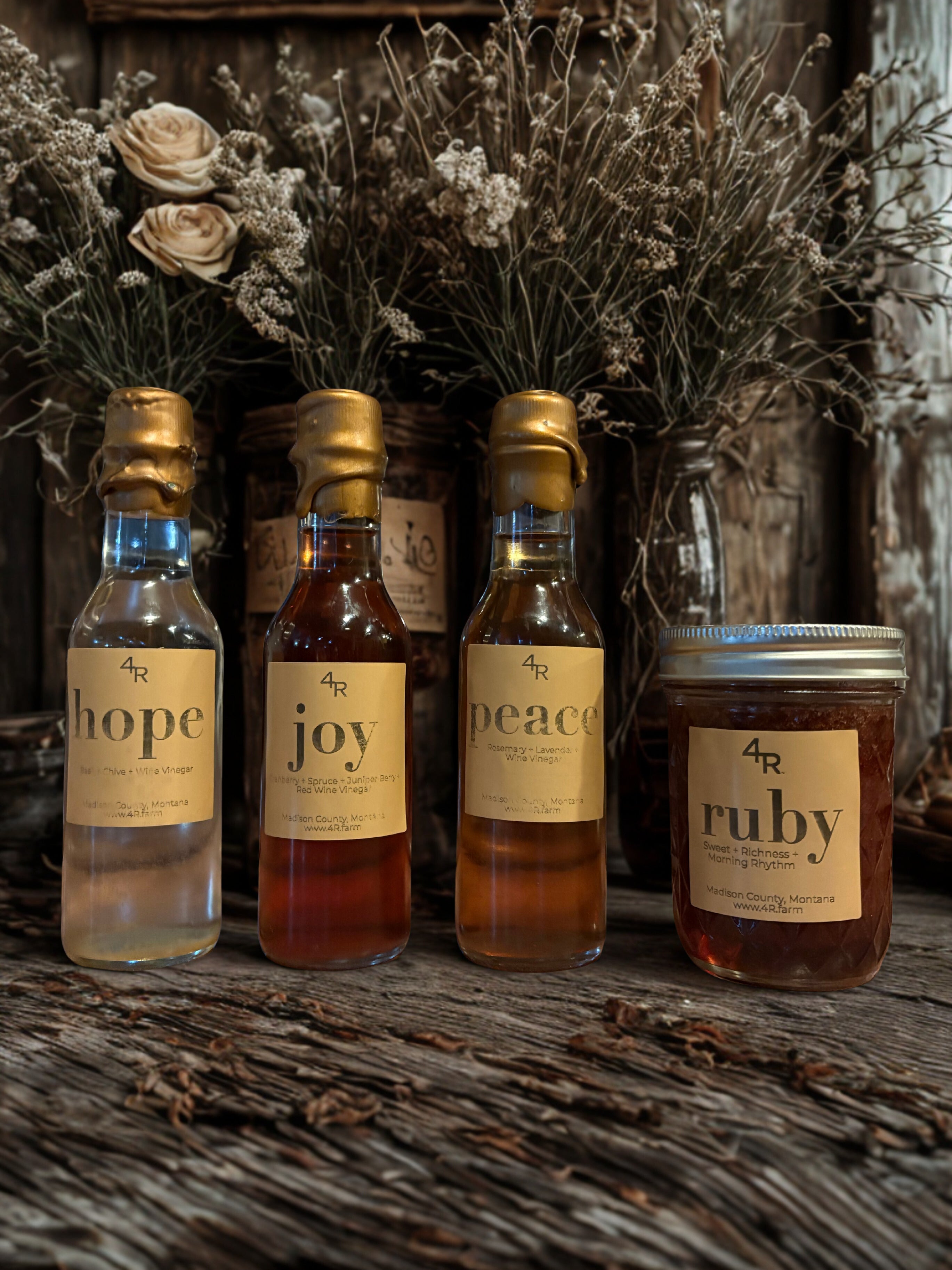 Four bottles labeled 'hope', 'joy', 'peace', and a jar labeled 'ruby' on a rustic wooden surface with dried flowers in the background.