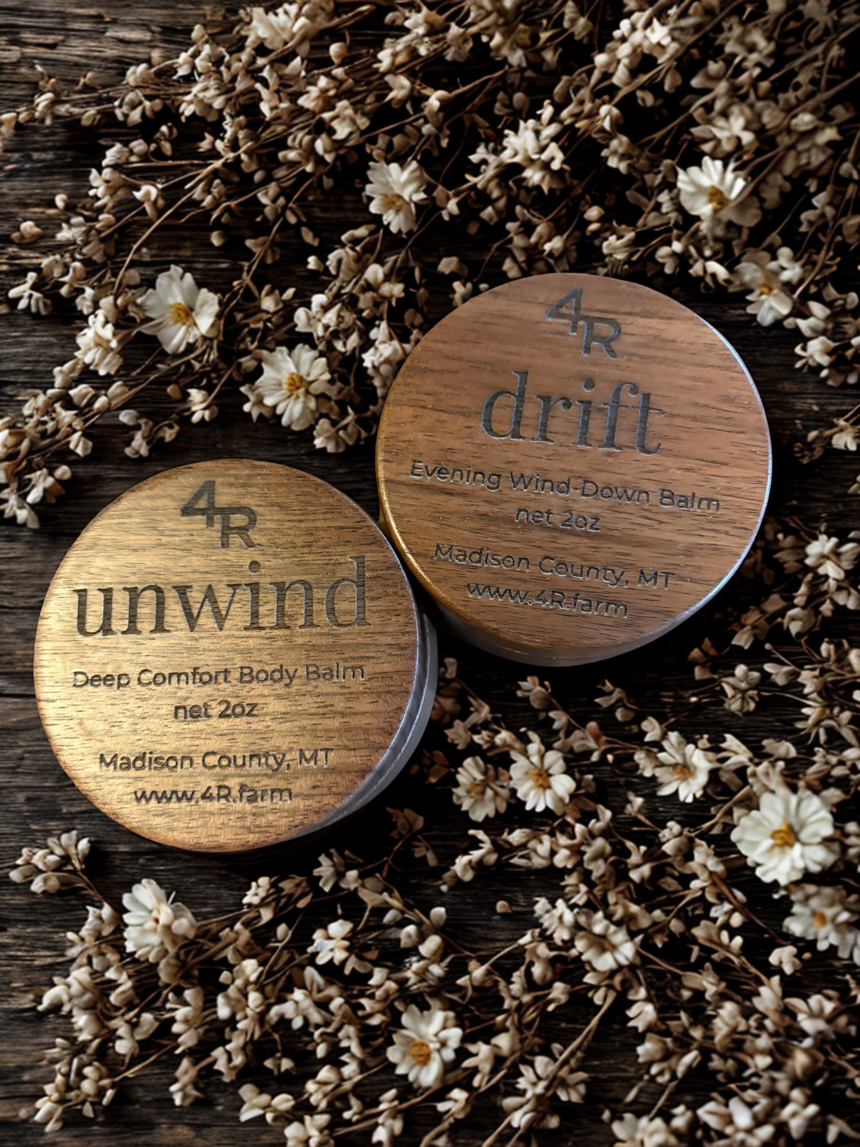 Two wooden containers labeled 'unwind' and 'drift' surrounded by dried flowers on a wooden surface.