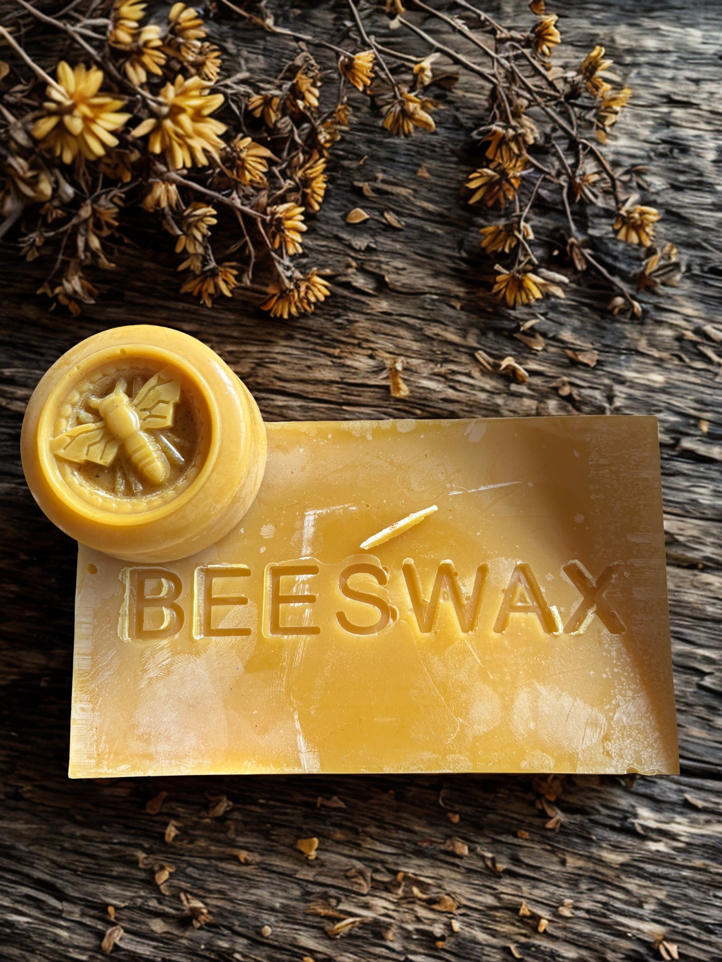 Beeswax bar with a stamp on a wooden surface with dried flowers.