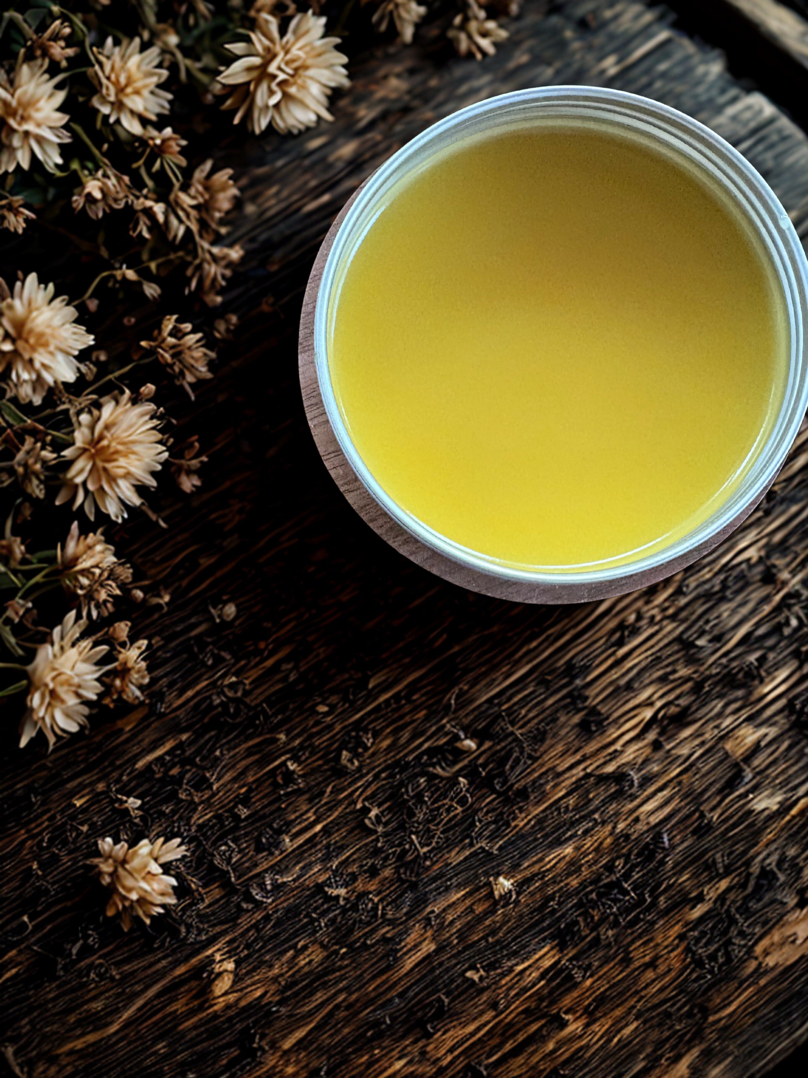 Jar of yellow cream on a wooden surface with dried flowers