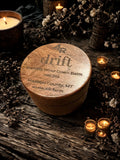 Round wooden container labeled '4R drift' on a rustic surface with candles and flowers.