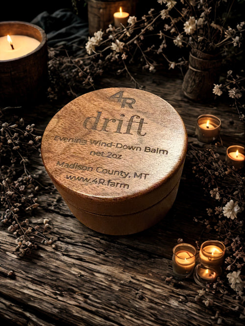 Round wooden container labeled '4R drift' on a rustic surface with candles and flowers.