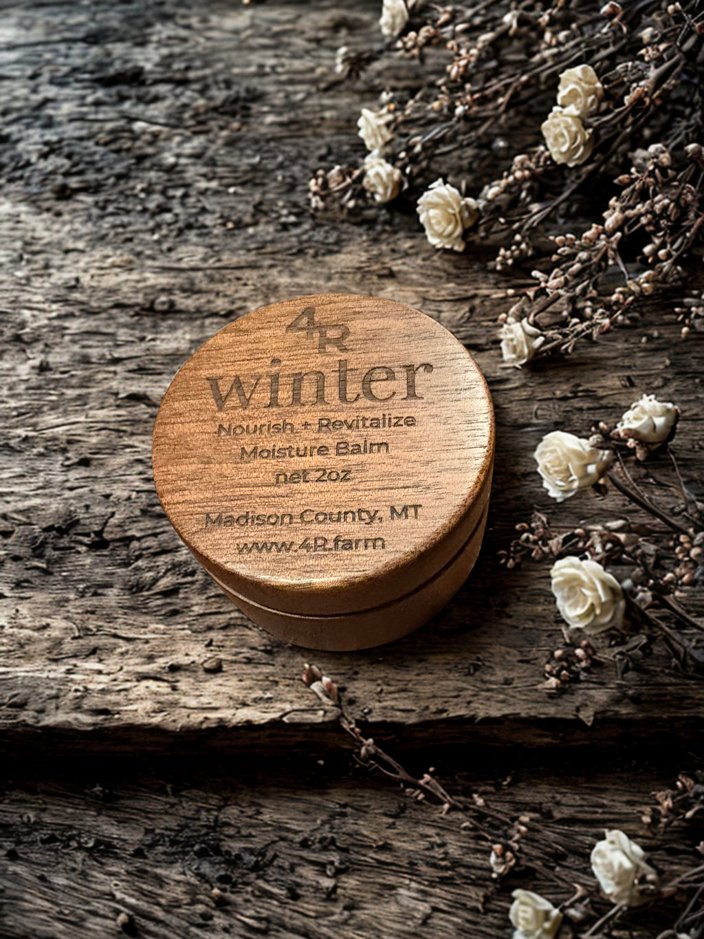 Wooden balm container labeled '4R winter' on a rustic wooden surface with flowers.