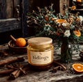Jar of 'tidings' spice mix on a wooden table with oranges and cinnamon sticks.