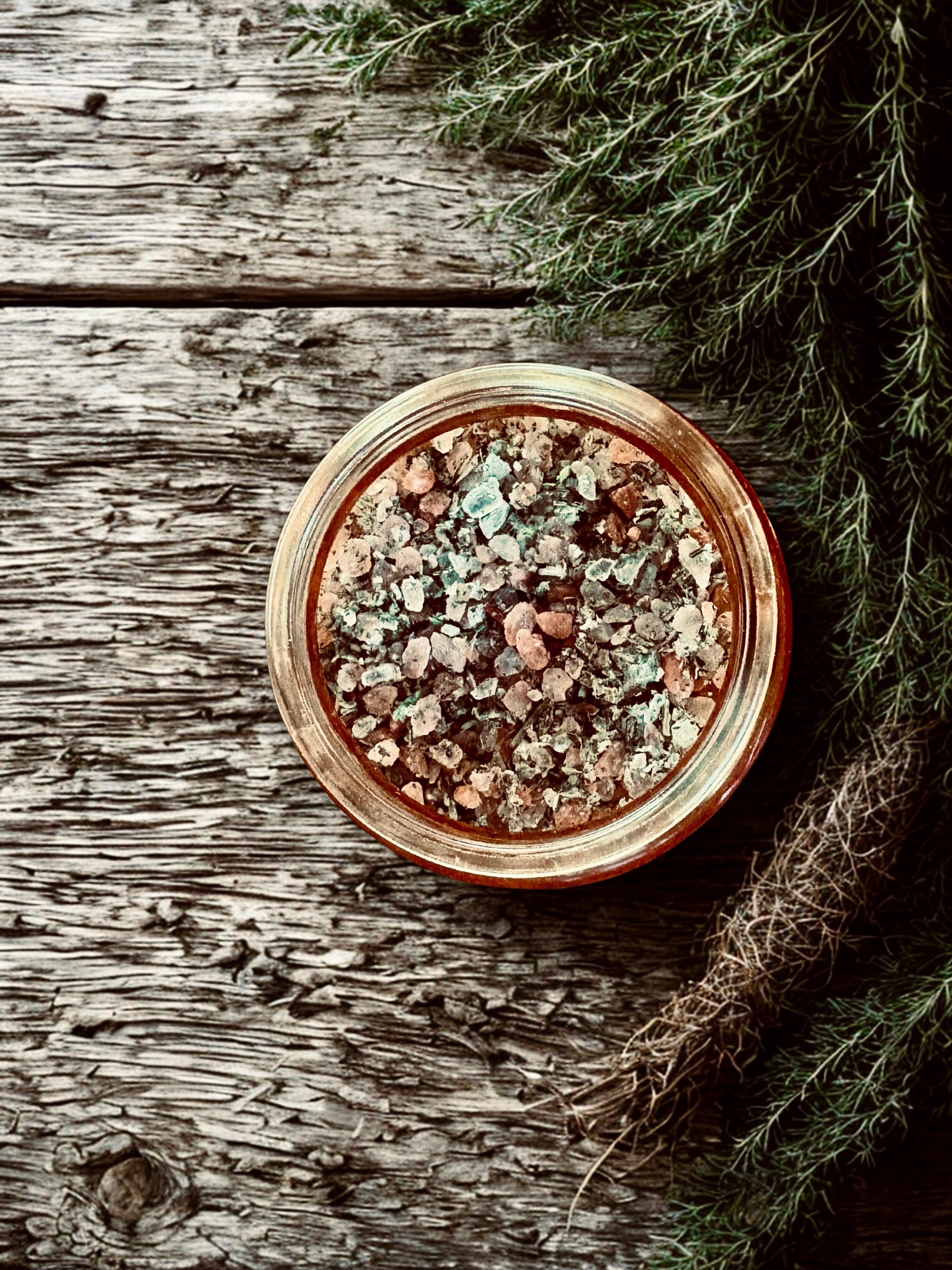 Jar of mixed herbs and salts on a wooden surface with greenery