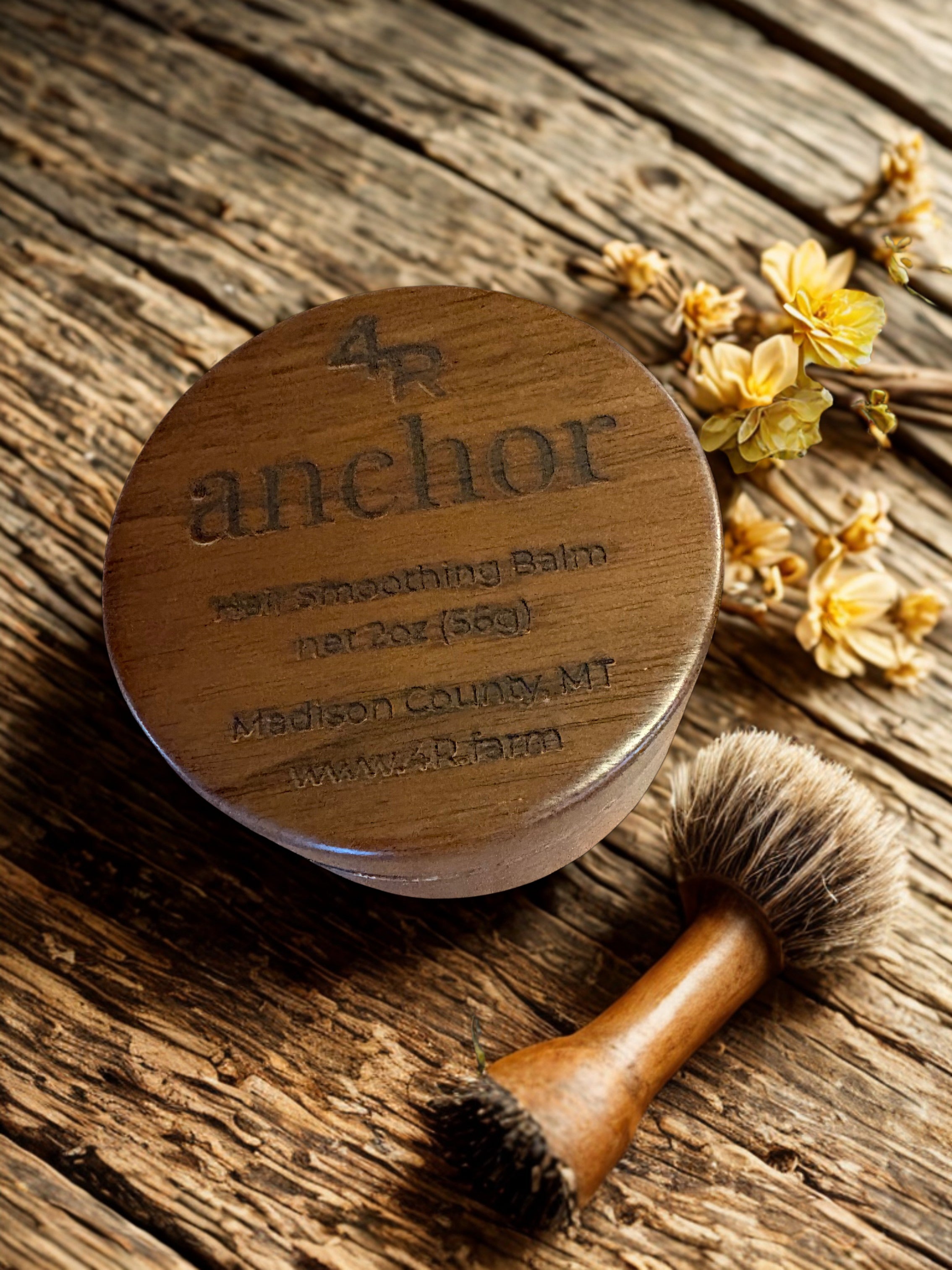 Wooden jar labeled 'anchor' with a brush on a wooden surface with flowers.