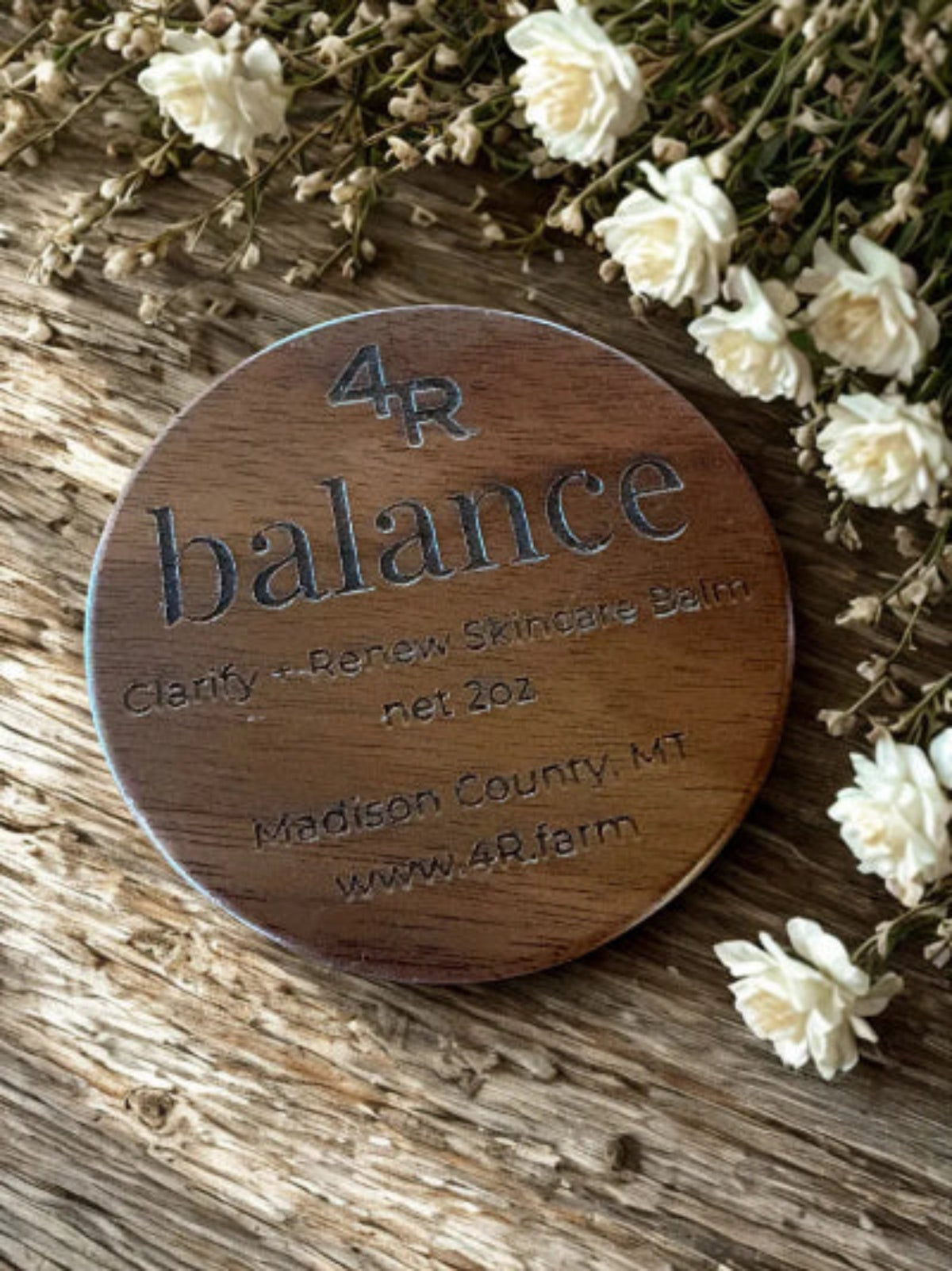 Wooden round product packaging labeled '4R balance' with white flowers around it.
