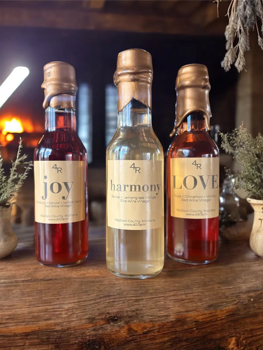 Three small bottles of 4R herb-infused vinegars on a wooden surface with 'joy', 'harmony', and 'love' labels.